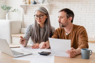 middle aged couple looking over documents on laptop